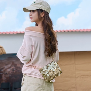 Sac bandoulière chic en paillettes dorées avec chaîne porté sur modèle avec ciel bleu