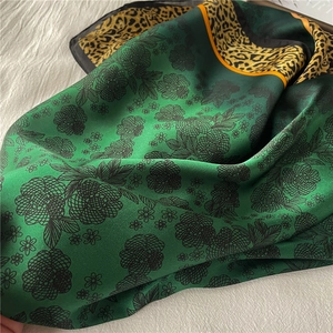 Close-up of emerald green silk scarf featuring black floral patterns and leopard print borders