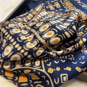 Close-up of folded satin scarf with orange and white geometric patterns on navy blue base
