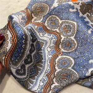 Detail of silk-like scarf featuring navy and orange paisley patterns with smooth texture
