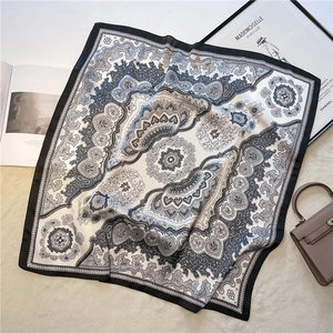 Detail of elegant paisley print silk square scarf styled on a white plush rug backdrop