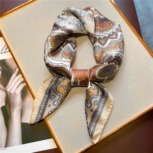 Close-up of paisley silk scarf with orange and cream patterns on a golden tray