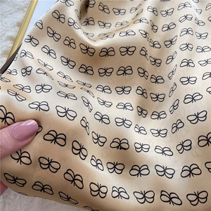 Detailed close-up of champagne silk scarf featuring black butterfly prints and soft texture