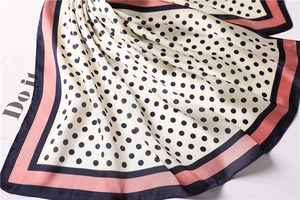 Detailed view of silk-like square scarf with black polka dots and pink contrast borders