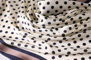 Close-up of silk-like scarf featuring classic polka dots and elegant striped border detail