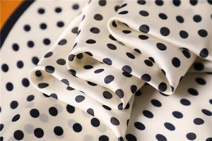 Macro detail of creamy white silk scarf featuring black polka dots and satin texture
