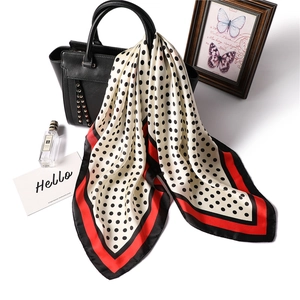 Polka dot silk scarf with red and black borders draped on a leather handbag accessory