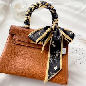 Sac à main en cuir marron avec foulard en soie noir et jaune entouré sur l'anse