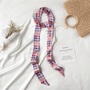 Détail d'un foulard en soie rose à motif chat stylisé sur robe blanche avec accessoires