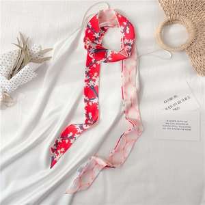 Détail d'un foulard twilly rouge à fleurs noué sur une robe en satin blanc élégante