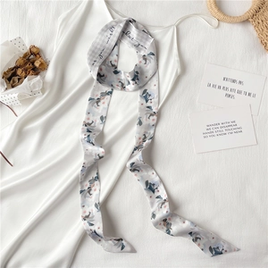 Détail d'une écharpe étroite en soie fleurie stylisée avec une robe en satin blanc