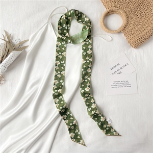 Détail d'un foulard étroit vert foncé à fleurs attaché à un sac en paille tressée