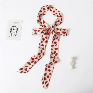 Elegant cream neck scarf with red heart prints tied in a bow next to art deco card