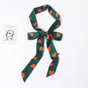 Dark green long narrow silk scarf with orange heart patterns tied in a bow on white desk