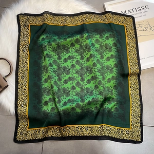 Elegant square silk scarf with green floral center and leopard print border on plush mat