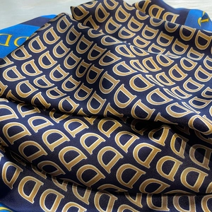Dettaglio macro di una sciarpa in seta blu scuro con motivi di lettere D dorate