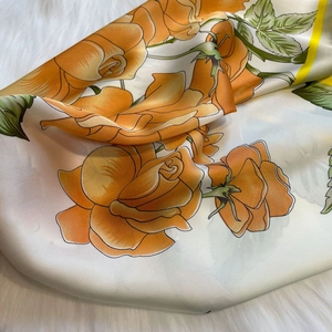 Close-up of elegant silk-like square scarf with vibrant orange-yellow rose floral prints