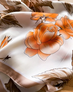Close-up of ivory silk scarf with orange rose print and smooth satin texture detail
