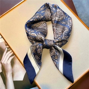 Detail of navy and beige paisley silk scarf tied as a bow on a luxury gold tray