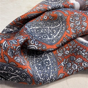 Detailed macro view of vintage orange paisley silk scarf with satin texture and soft sheen