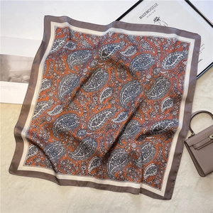 Detail shot of vintage paisley print silk scarf in orange and blue on a soft white surface