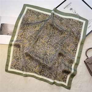 Detail of green paisley silk scarf with intricate vintage pattern on a soft beige carpet