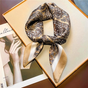 Detailed close-up of brown paisley silk square scarf with floral patterns on a display tray
