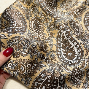 Close-up of vintage paisley silk scarf fabric showing smooth texture and golden tones