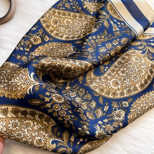 Macro detail of silk-like paisley satin scarf showing navy and gold floral patterns