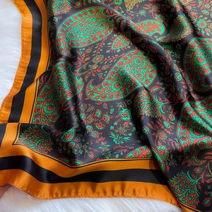 Detailed close-up of glossy paisley silk scarf with orange borders on white faux fur
