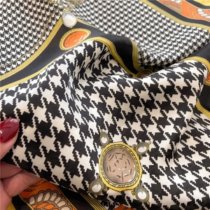 Macro detail of houndstooth silk scarf showing orange borders and equestrian motifs