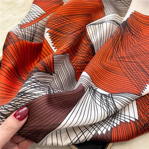 Close-up of geometric silk scarf with orange and brown lines held by hand