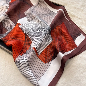 Detail of silk square scarf featuring orange geometric patterns on a plush surface