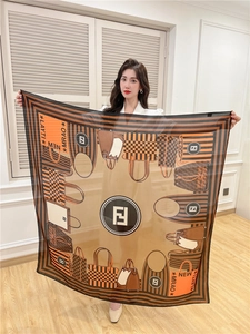 Detail of a large orange and brown square silk scarf with vintage prints worn by a model