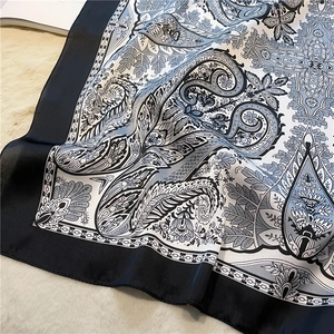Detail of navy paisley print silk scarf with satin finish on soft white plush background