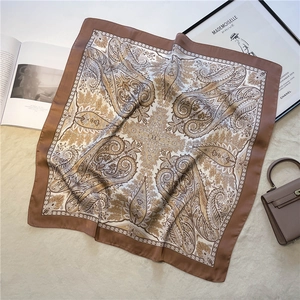 Detail of brown paisley silk scarf styled with a luxury handbag on a soft background