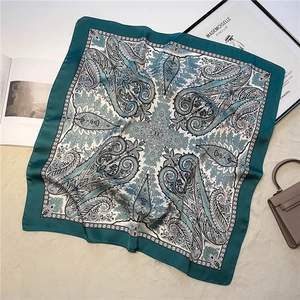 Detail of green paisley silk square scarf with vintage pattern on a soft textured surface
