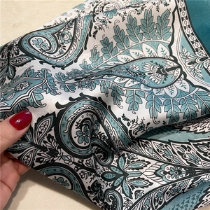 Detailed macro view of teal paisley pattern silk scarf with elegant floral print details