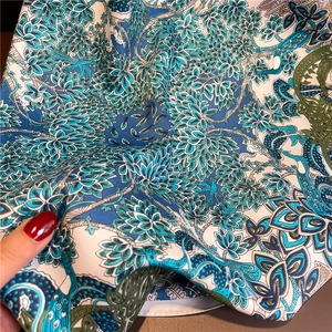 Gros plan détaillé des motifs d'ailes de paon et fleurs sur un foulard en soie bleue