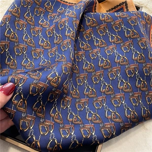 Detail of luxury navy silk scarf with horse stirrup patterns and orange rolled edges