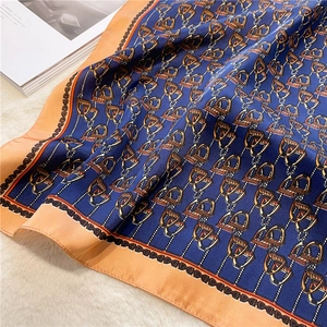 Detail of luxury silk scarf with equestrian stirrup print in navy blue and orange