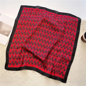 Detail view of 70cm red silk scarf with luxury bag pattern on soft plush surface