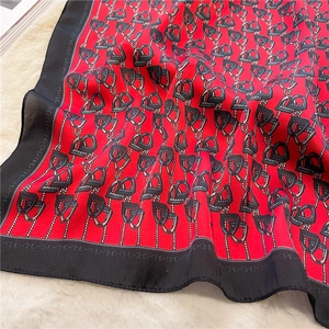 Detailed close-up of luxury red silk scarf featuring equestrian stirrup and chain patterns