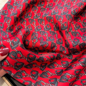 Detailed close-up of red silk square scarf with classic horsebit and rope pattern print