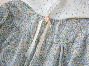 Détail d'une robe fleurie pour fille avec col en dentelle, revers à pois et fleur rose