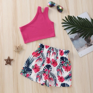 Flat lay of girl's summer set with fuchsia one-shoulder top and floral tropical shorts