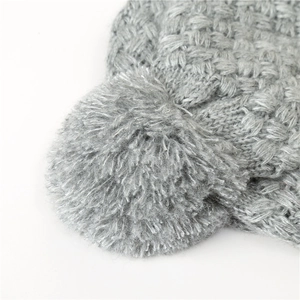 Close-up of grey knitted winter hat showing thick yarn texture and soft pom-pom detail