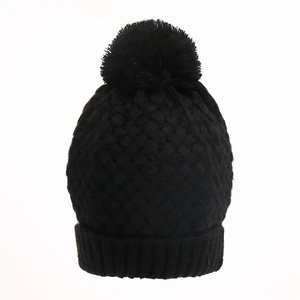 Close-up of black cable knit beanie featuring soft faux fur pom-pom and ribbed cuff