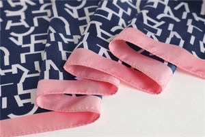 Close-up of silk-feel scarf with navy blue letters and pink border detail