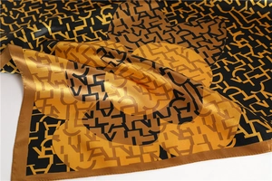 Close-up of golden and black satin scarf showing letter print and silk-like texture